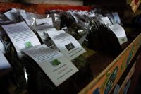 Varias bolsas pequeñas conteniendo yuyos con etiquetas que dicen lo que hay en cada una; además aparece el nombre de Ana Lanouguere y la marca Medicinas del Queguay.