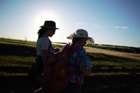 Emilia y Ana caminan por el campo, con el sol a un costado; Ana carga con una gran mochila roja.