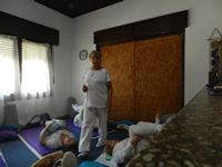 Blanca habla a varias mujeres de edad avanzada que están acostadas en el suelo haciendo ejercicios de yoga.