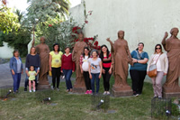 En un patio grande, Delfa, varias mujeres y una niña posan para la foto paradas junto a cuatro estatuas de mujeres.
