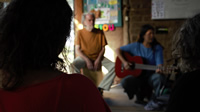 Con su guitarra, Mariana anima una ronda en la que otras mujeres también cantan; a su lado un hombre canoso de barba sentado sobre un cajón peruano.